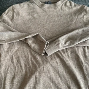 Beige tröja från H&M - Säljer en stilren beige tröja från H&M i slim fit. Tröjan är tillverkad i 100% bomull och har långa ärmar med ribbade muddar. Perfekt för en avslappnad och snygg look.