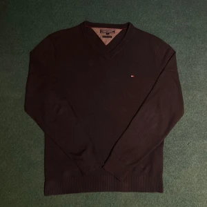 Svart tröja från Tommy Hilfiger - Säljer en stilren svart tröja från Tommy Hilfiger i fin bomullskashmirblandning. Tröjan har en v-ringad hals och ett diskret broderat logotypmärke på bröstet. Perfekt för en klassisk look.