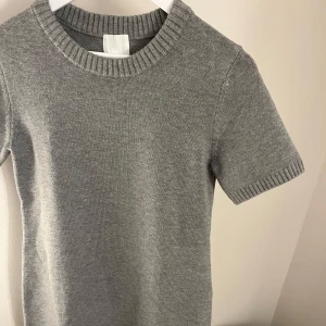 Grå stickad klänning  från H&M - Säljer en stilren grå stickad klänning från H&M. Klänningen har korta ärmar och en rund halsringning med ribbade kanter. Har aldrig fått använda den och därför säljer jag den nu vidare💕