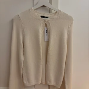 Offwhite kofta från Gina Tricot - Säljer en stilren offwhite kofta från Gina Tricot. Den har en enkel knapp framtill och är perfekt för lager-på-lager. Koftan är långärmad och gjord i ett mjukt material som passar bra till både vardag och fest. Perfekt för höst och vår!