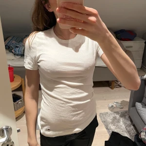 Vit t-shirt från Tommy Hilfiger - Säljer en klassisk vit t-shirt från Tommy Hilfiger. Den är kortärmad och tillverkad i mjukt bomullsmaterial. Perfekt för en enkel och stilren look. Passar bra till jeans eller shorts.