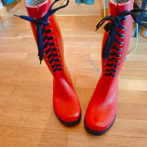 stövlar ( Långa/höga)från Ellos Röda, svart snörning - Snygga röda stövlar från Ellos med svarta snören och robust sula.     Perfekta för regniga dagar och ger en färgklick till din outfit.     Stövlarna har en klassisk design med snörning framtill.    Fungerar lika bra som skor till en Carrie Bradshaw outfit med klänning, eller vardags outfit med jeans.. som till skogspromenad och även i stallet,  p.ga. lätt upphöjda " klacken". Eller på festival.. helt vattentäta och ny impregnerat. .. med andra ord.. stövlar med 5 användnings möjligheter minst! 