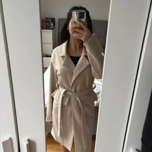 Beige kappa från BikBok - Säljer denna kappa från Bik bok då den ej kom till användning , nästan helt ny i storlek xs. Man kan välja att stänga den med skärpet eller med knappen