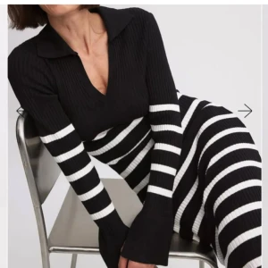 Svart och vit randig klänning - Snygg svart och vit randig klänning med ribbad struktur och v-ringad krage. Klänningen har långa ärmar och en figurnära passform som ger en stilren look. Perfekt för en trendig outfit.