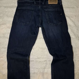 Replay anbass jeans mörkblå - Snygga mörkblå jeans från Replay med klassisk femficksdesign och knappgylf. Perfekta för en stilren look. Märkeslapp baktill och diskreta sömmar ger en tidlös känsla. Size 30 Midja 34Längd