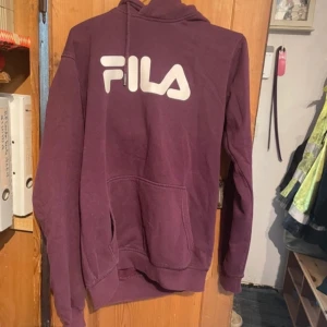 Vinröd hoodie från FILA - Säljer en vinröd hoodie från FILA med stor vit logga på bröstet. Tröjan har en klassisk känguruficka och långa ärmar. Perfekt för en avslappnad stil.