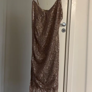 Glittrig champagnefärgad klänning - Säljer en glittrig champagnefärgad klänning med smala axelband och fransdetaljer längst ner. Perfekt för en festlig kväll! ✨