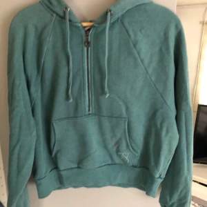 Turkos/grön hoodie från Victoria's Secret - Säljer en snygg grön hoodie från Victoria's Secret med dragkedja och känguruficka. Den har en croppad passform och långa ärmar. Perfekt för en avslappnad stil. 💚
