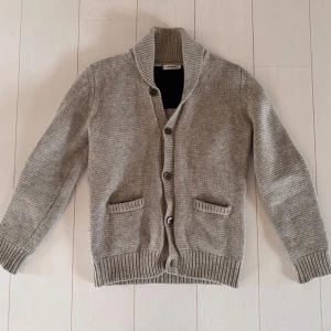 Beige stickad kofta från J.Lindeberg - Säljer en riktigt fin beige stickad kofta från J.Lindeberg i 100% lammull. Koftan har en klassisk design med knappar framtill och två praktiska fickor. Perfekt för kyliga dagar och ger en snygg touch till din outfit. Mycket fint skick, knappt använd. Priset är inte hugget i sten! 