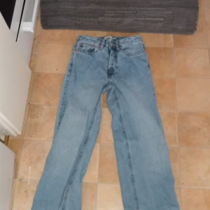 Blå jeansbyxor - Säljer ett par klassiska blå jeansbyxor med fem fickor och knappgylf. De har en rak passform och är perfekta för en avslappnad stil.