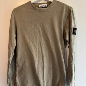 Stone Island tröja - Säljer en olivgrön långärmad tröja från Stone Island. Tröjan har en rund halsringning och det ikoniska Stone Island-märket på ärmen. Perfekt för en stilren och avslappnad look.