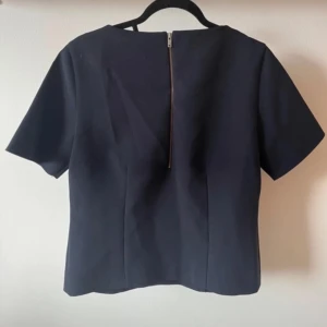 Mörkblå kortärmad topp med dragkedja - Snygg mörkblå topp med korta ärmar och en dragkedja i ryggen. Perfekt för en stilren look.