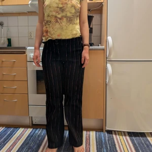 Svarta randiga byxor med knappar - Köpt här på Plick! Snygga svarta byxor med rosa och vita ränder. Byxorna har en hög midja och stängs med knappar framtill. Perfekta för en stilren look. Skulle säga storlek 38!!