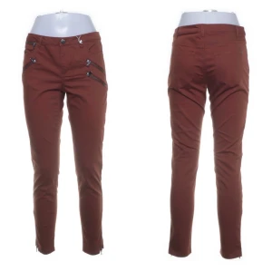 Nyskick! Bruna byxor från Saint Tropez - Snygga byxor från Saint Tropez i storlek M. Byxorna har en normal passform med dragkedjor som detaljer framtill. Tillverkade i en blandning av bomull, polyester och spandex för en bekväm känsla. Perfekta för en stilren look. Knappt använda i nyskick.