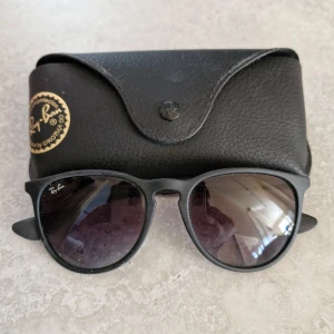 Svarta solglasögon från Ray-Ban - Snygga svarta solglasögon från Ray-Ban med rundad form och mörka linser. Perfekta för en stilren look. Kommer med ett svart fodral för säker förvaring. Köpta på flyget, äkta.