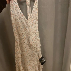 Blommig klänning från Nelly - Säljer en söt blommig klänning från  Nelly. Klänningen är ärmlös med volangdetaljer och har en ljus bas med små blommor i olika färger. Perfekt för sommarens alla tillfällen! Helt oanvänd, stretchigt material så passar både en M som en S