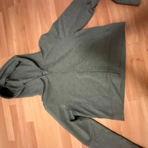 Grå hoodie med dragkedja - Säljer en stilren grå hoodie med dragkedja och huva. Perfekt för en avslappnad look. Den har långa ärmar och en bekväm passform.