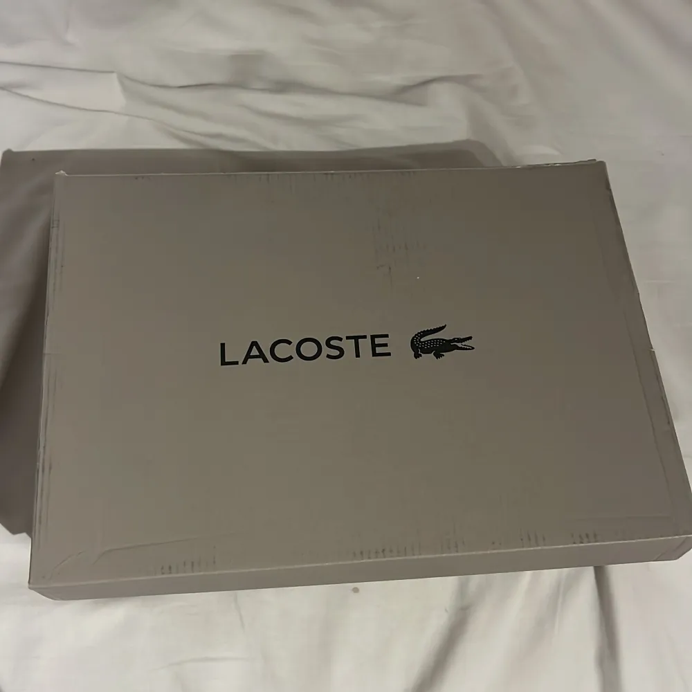 Snygga vita sneakers från Lacoste med klassisk design. Skorna har snörning och den ikoniska krokodilloggan på sidan. Perfekta för en stilren look.. Kengät.