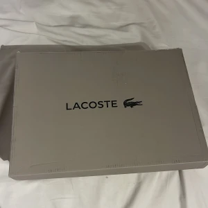 Vita sneakers från Lacoste helt nya inte ens använda  - Snygga vita sneakers från Lacoste med klassisk design. Skorna har snörning och den ikoniska krokodilloggan på sidan. Perfekta för en stilren look.