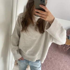 Beige stickad tröja - Mysig beige stickad tröja med polokrage och långa ärmar. Perfekt för kyligare dagar med sin avslappnade passform och ribbade detaljer vid ärmslut och nederkant. En stilren och bekväm tröja för alla tillfällen.