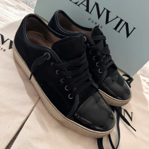 Marinblåa  sneakers från Lanvin - Snygga mörkblåa sneakers från Lanvin med glansig tå och snörning. Skorna har en vit sula som ger en stilren kontrast. Perfekta för en trendig look.