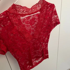 Röd spetsblus - Säljer en vacker röd spetsblus med korta ärmar och v-ringning. Perfekt för att lägga till en touch av elegans till din outfit. Blusen är genomskinlig och har ett fint blommönster. Storlek S❤️