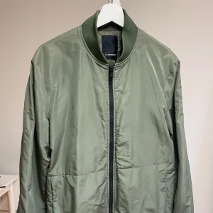 Grön vår/bomberjacka från J.Lindeberg - Snygg grön vårjacka från J Lindeberg. Jackan har en klassisk bomberstil med ribbade muddar vid ärmslut och nederkant. Jackan är i väldigt bra skick.
