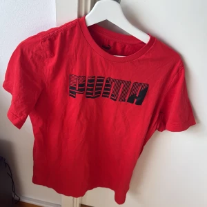 Röd t-shirt från Puma - Säljer en röd t-shirt från Puma med ett stort tryck på framsidan. T-shirten har korta ärmar och en rund halsringning. Perfekt för en sportig look eller vardagsbruk.