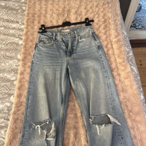 Ljusa jeans med slitningar - Säljer ett par ljusa jeans med coola slitningar på knäna. De har en klassisk femficksdesign och en avslappnad passform. Perfekta för en trendig och avslappnad stil. De är för korta för mig som är 174cm