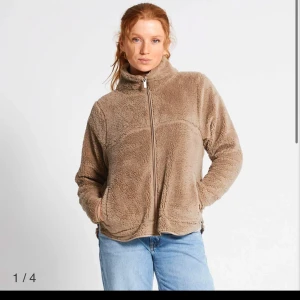 Fleece - Mysig beige fleece med dragkedja framtill. Perfekt för kyliga dagar med sin fluffiga och varma design. Tröjan har en hög krage och långa ärmar, vilket gör den extra bekväm och skyddande mot vind.