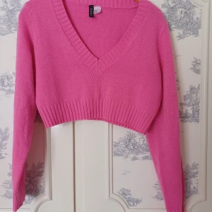 Rosa croppad tröja från Divided - Säljer en snygg rosa croppad tröja från Divided. Tröjan har en v-ringad design och långa ärmar med ribbade muddar. Perfekt för en trendig look! 💖