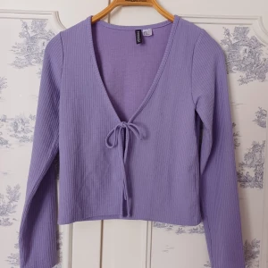 Lila ribbad kofta från H&M - Säljer en lila ribbad kofta från H&M med knytning framtill. Den har en v-ringad design och långa ärmar, perfekt för en stilren look. Passar bra till både jeans och kjol. 💜