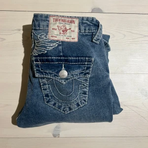 Blåa jeans från True Religion😍 - INTRESSEKOLL!! Snygga lågmidjade blåa bootcut jeans från True Religion i storlek W25 med en snygg detalj på baksidan. Jeansen är nästan aldrig använda och är i perfekt skick🥰innerbenslängden är 81 cm🥰