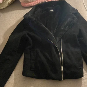 Svart jacka med pälsdetaljer - Jätte snygg svart vår jacka i super bra skick perfekt till våran för en stilren look. Jackan har en dragkedja framtill och är långärmad.