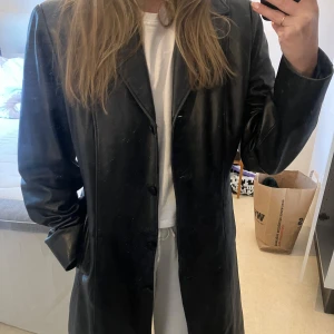 Svart skinnkappa från Saki - Snygg svart skinnkappa från Saki med knappar framtill. 