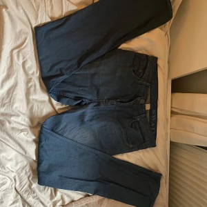 Blå jeans från Burberry Brit - Snygga blå jeans från Burberry Brit med klassisk design. De har en rak passform och är tillverkade i ett slitstarkt denimtyg. Byxorna har knappar och en stilren läderdetalj med logotyp på baksidan. Perfekta för en stilren look.                                                                     Använda storlek S