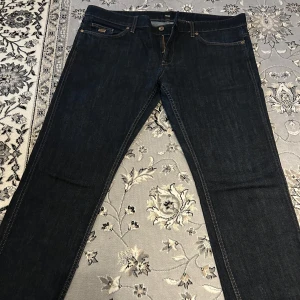 Mörkblå jeans från Hugo Boss - Snygga mörkblå jeans från Hugo Boss med klassisk femficksdesign och knappgylf. Perfekta för en stilren look. Märkeslappen syns tydligt på insidan. Säljs pågrund av dem blivit för stora på mig. Priset kan diskuteras!