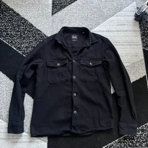 Svart overshirt från Only & Sons - Säljer en svart overshirt från Only & Sons med klassisk krage och två bröstfickor med lock och knappar. Skjortan har långa ärmar och stängs med knappar framtill. Perfekt att bära som lager över en t-shirt. Sitter stilrent, pris kan diskuteras 