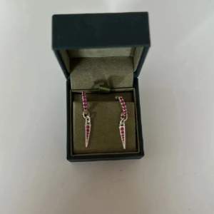 Säljer ett par coola silverfärgade örhängen med små rosa stenar och en spetsig hängande detalj. Perfekta för att ge din look lite edge och färg. Passar dig som gillar unika smycken! Orginalpris: 400kr/styck (800kr/par)