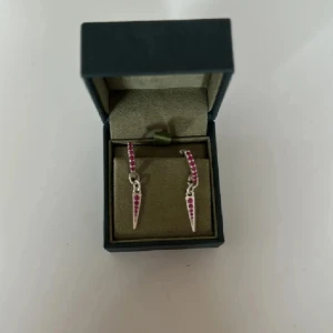 L8h örhängen  - Säljer ett par coola silverfärgade örhängen med små rosa stenar och en spetsig hängande detalj. Perfekta för att ge din look lite edge och färg. Passar dig som gillar unika smycken! Orginalpris: 400kr/styck (800kr/par)