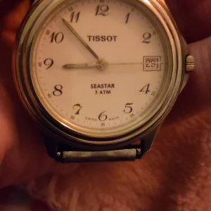Tissot Seastar herrklocka med vit urtavla - Klassisk Tissot Seastar herrklocka med rund silverfärgad boett och vit urtavla. Klockan har tydliga svarta siffror, datumfönster vid kl 3 och silverfärgade visare. Vattentät till 3 ATM. 