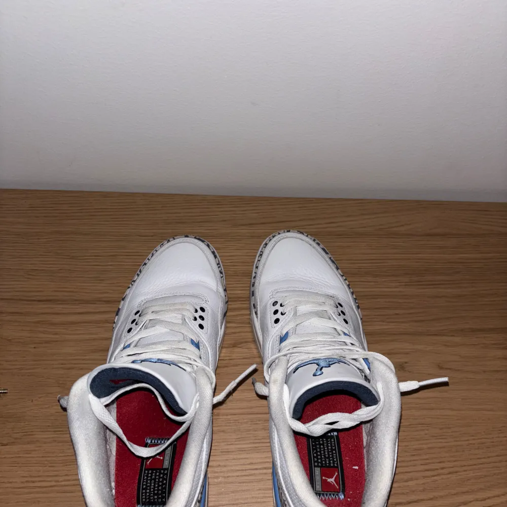 Säljer ett par Nike Air Jordans 3 Retro UNC med vit ovandel i skinn, ljusblå detaljer och klassiskt elefantmönster vid tå och häl. Skorna har snörning, rund tå och synlig Air-enhet i sulan. Perfekta för dig som gillar sneakers med unik stil.. Kengät.