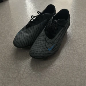 Nike phantom custom made limited edition  - Snygga fotbollsskor från Nike i grått och svart med ett subtilt mönster och blå detaljer. Skorna har snörning och är designade för optimal prestanda på planen.