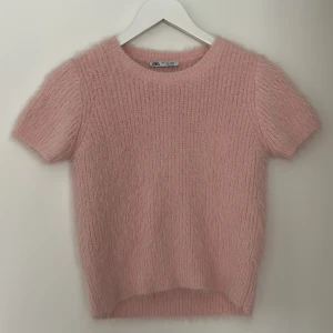 Rosa stickad tröja från Zara - Säljer en söt rosa stickad tröja från Zara. Tröjan har korta ärmar och en mjuk, fluffig textur som ger en mysig känsla. Perfekt för att lägga till en touch av färg och stil till din garderob.