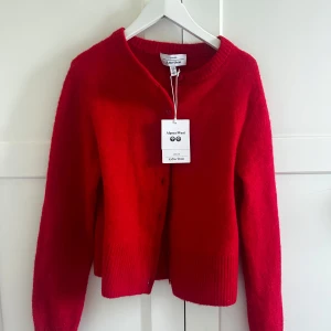 Röd stickad kofta från & Other Stories - Snygg röd kofta i alpackaull från & Other Stories. Den har en klassisk design med knappar framtill och ribbade kanter. Helt ny aldrig använd. Går ej ner i pris 