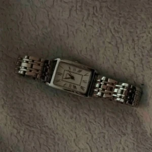 Silverfärgad fyrkantig klocka med länkarmband - Stilren klocka med fyrkantig urtavla och romerska siffror. Klockan har ett silverfärgat metallarmband i länkdesign och klassisk look. Perfekt accessoar. köpte på plick för 350kr, aldrig använt 