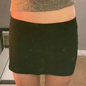 Svart kortkjol från Boohoo - Enkel svart kortkjol från Boohoo i stretchigt material. Kjolen har en tight passform och är perfekt för dig som gillar minimalistisk stil. Resår i midjan för extra komfort. Snygg att matcha med crop tops eller oversized tröjor.