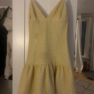 Gul klänning med struktur från ASOS DESIGN - Säljer en ljusgul klänning från ASOS DESIGN med v-ringad hals och markerad midja. Klänningen har en strukturerad yta och är ärmlös med en voluminös kjol. Perfekt för vår och sommar!
