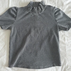 Polotopp från Zara - Säljer en svartvit topp från Zara med hög volangkrage och korta ärmar. Använd ett fåtal gånger och är perfekt till sommaren!