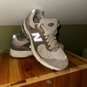 Beige och bruna sneakers från New Balance - Säljer ett par klassiska New Balance sneakers i beige och brunt med vit N-logga på sidan. Skorna har snörning och är tillverkade i en mix av mocka och syntetmaterial. Perfekta för vardagsstilen och riktigt bekväma att gå i. 